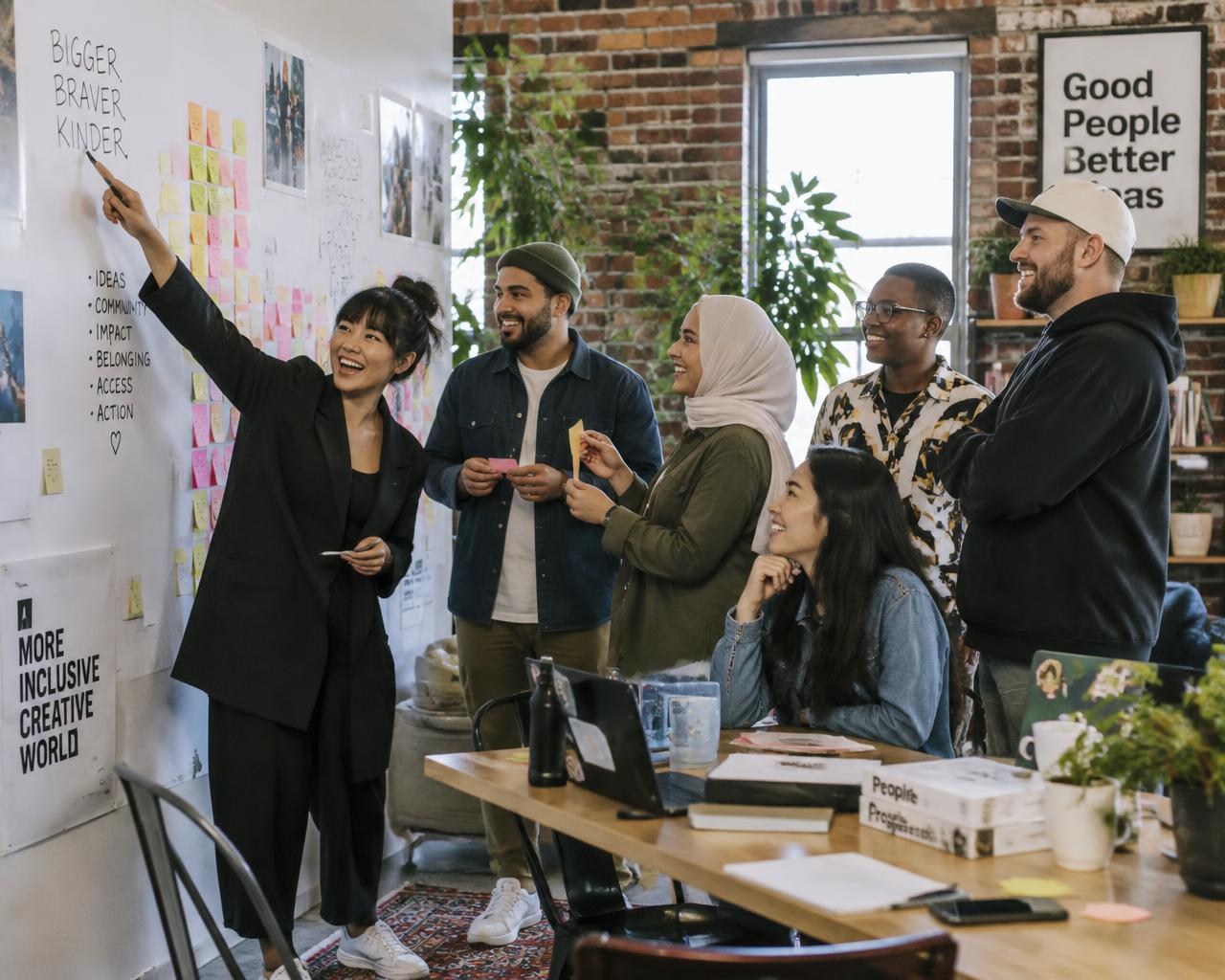 A diverse team laughing while building ideas on a sticky-note wall in a modern studio